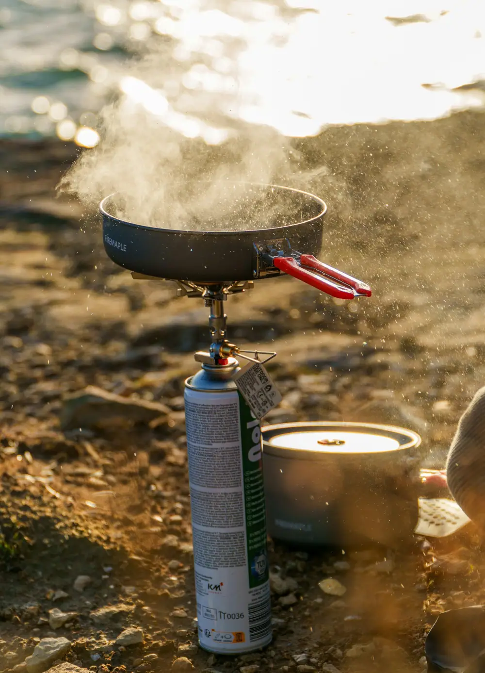 Steaming pot on a small portable camping stove set on rocky ground