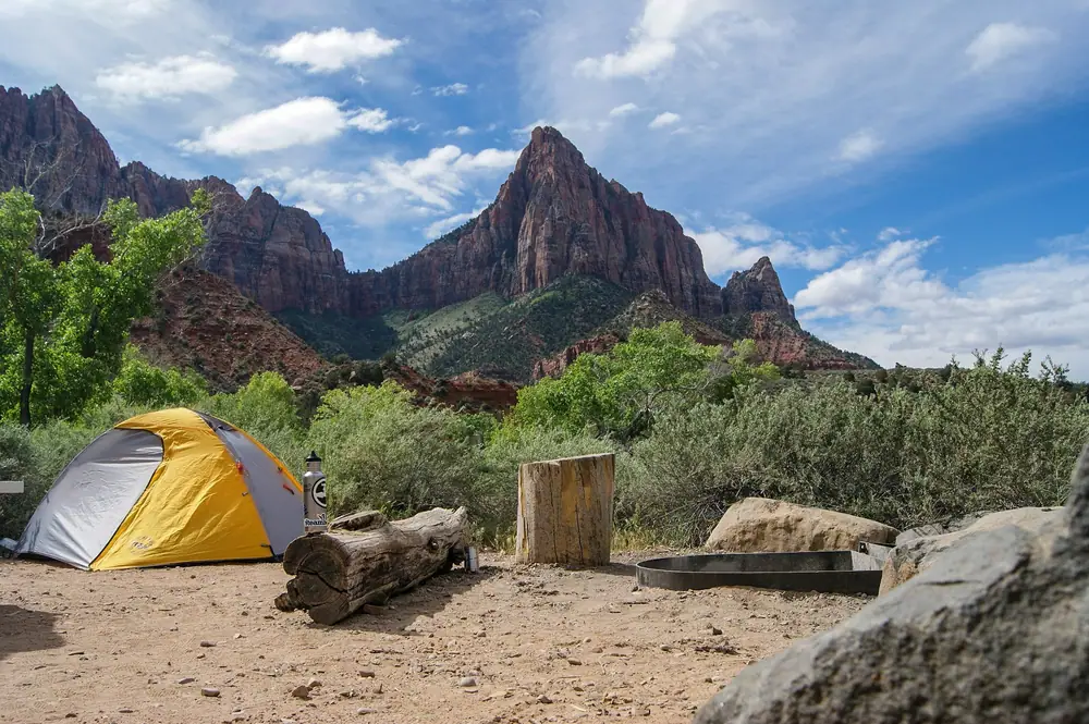 Yellow tent on a sandy campsite with a log bench below red rock cliffs
