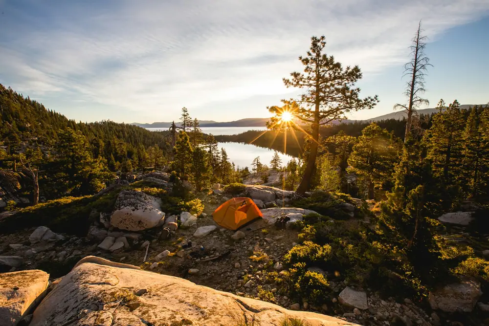 Sun setting over a lake framed by pine trees and granite boulders