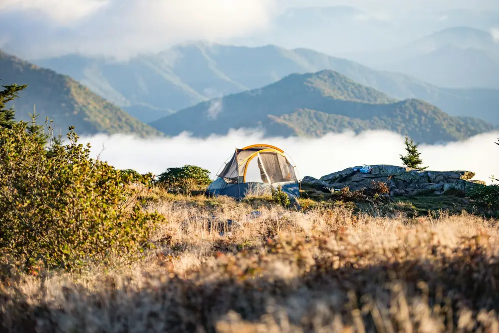 Small tent on a grassy ridge above a valley filled with low cloud