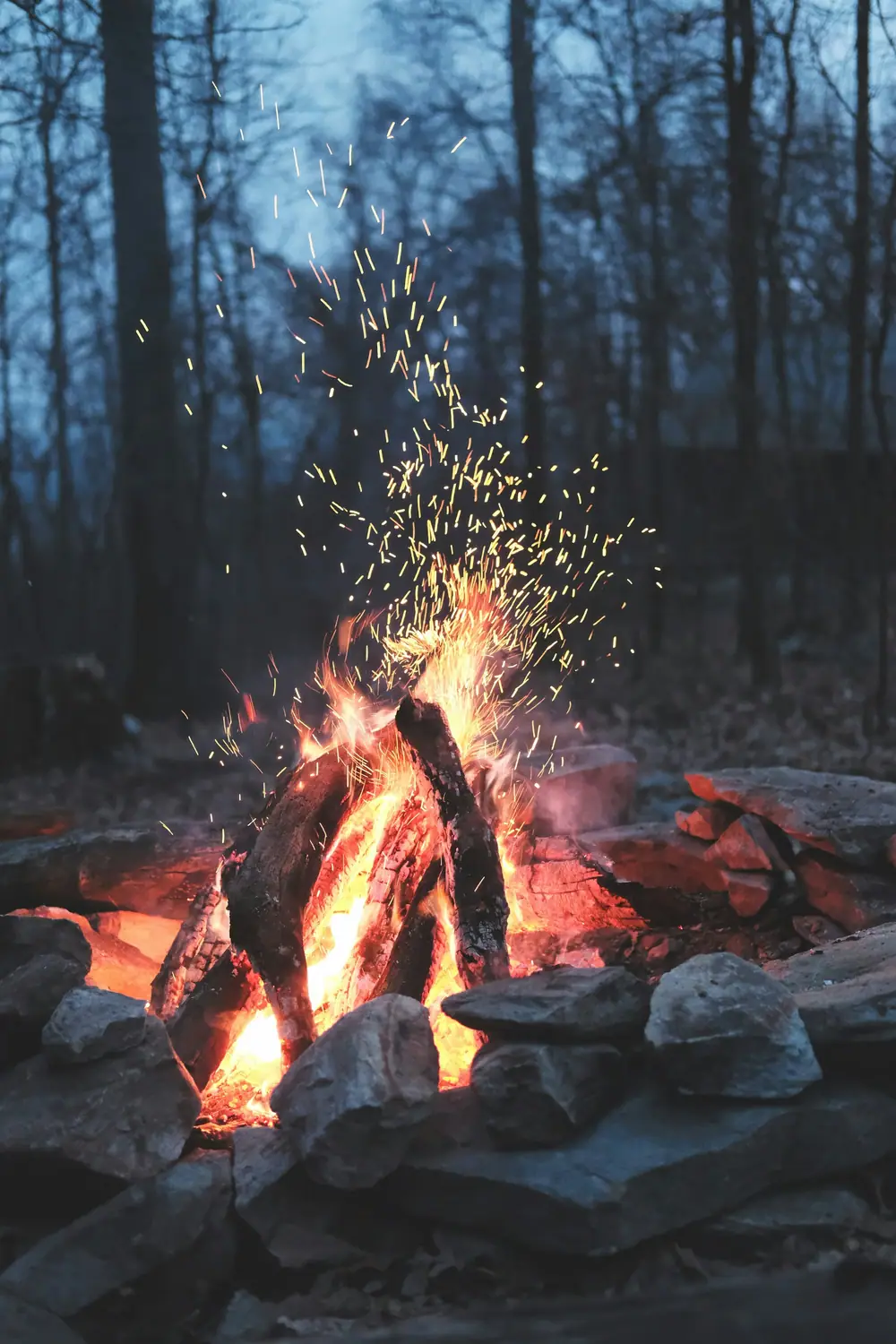 Close-up of a crackling campfire with sparks rising into the night
