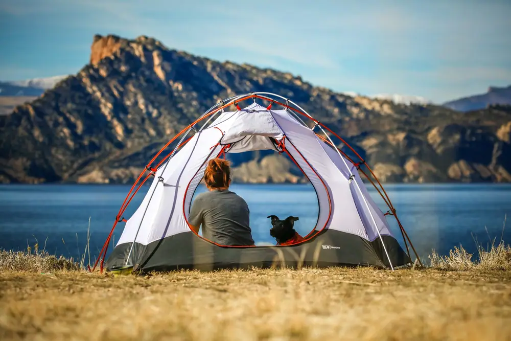 Person sitting in the doorway of a small dome tent pitched beside a mountain lake