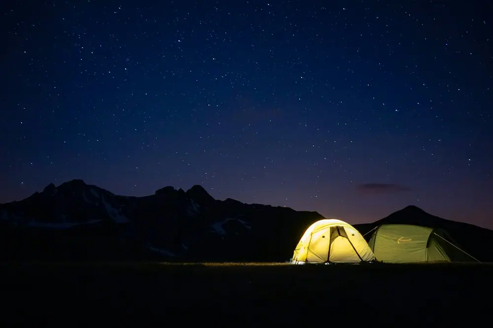 Two tents glowing softly under a starry night sky in the mountains